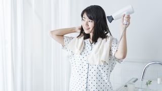 A woman dries her dark brown bob with a white hair dryer