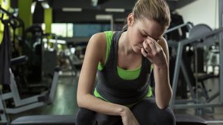 Woman sitting on a gym bench with her head in her hand looking stressed