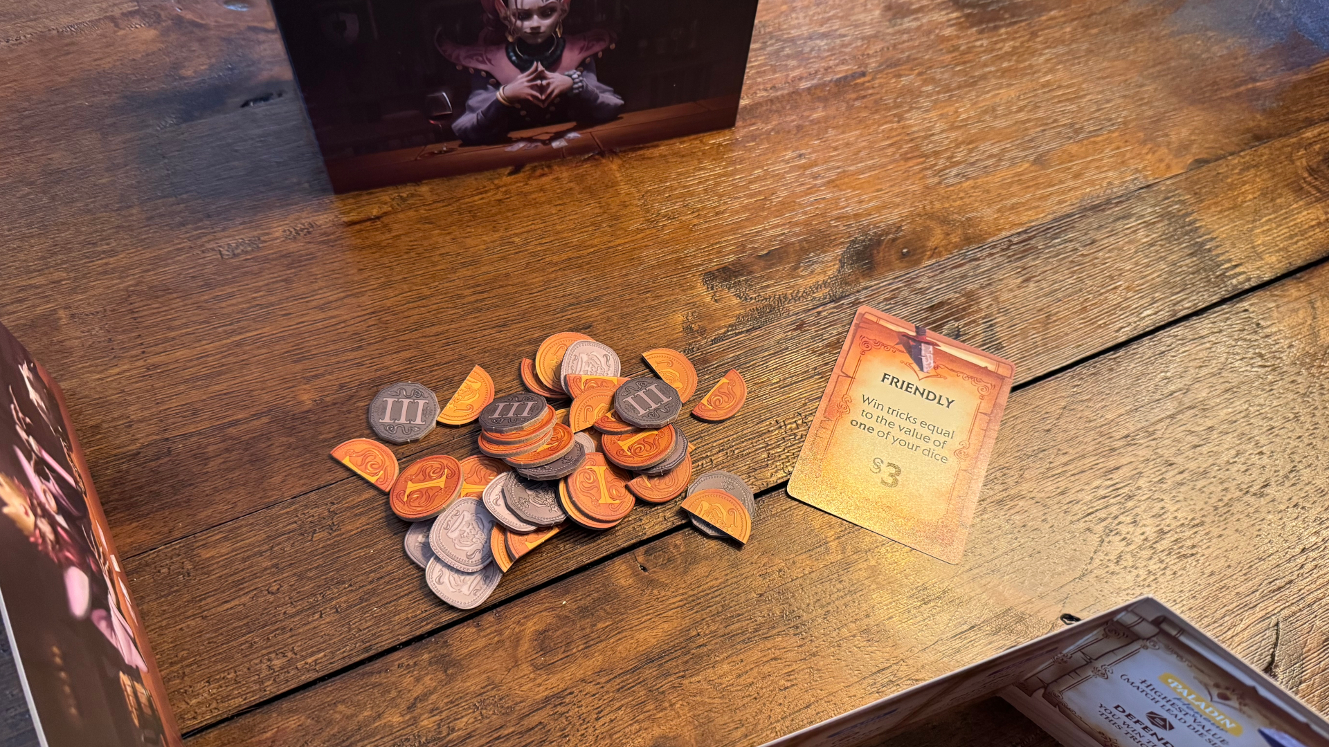 A small pile of coins beside a card on a wooden table, with player screens surrounding it