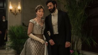 Carrie Coon as Bertha in a blue dress stands with Morgan Spector in a black dinner suit in The Gilded Age season 2.