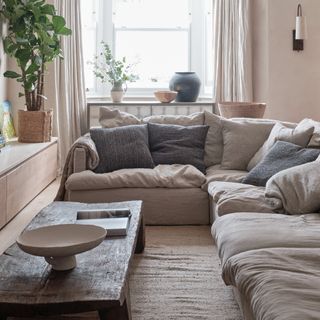 A living room with a large beige corner modular sofa and a textured wooden coffee table in front of it