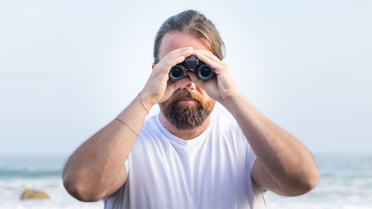 Nikon Stabilized 12x25 S binoculars held in the hands of the reviewer in front of breaking waves at the beach