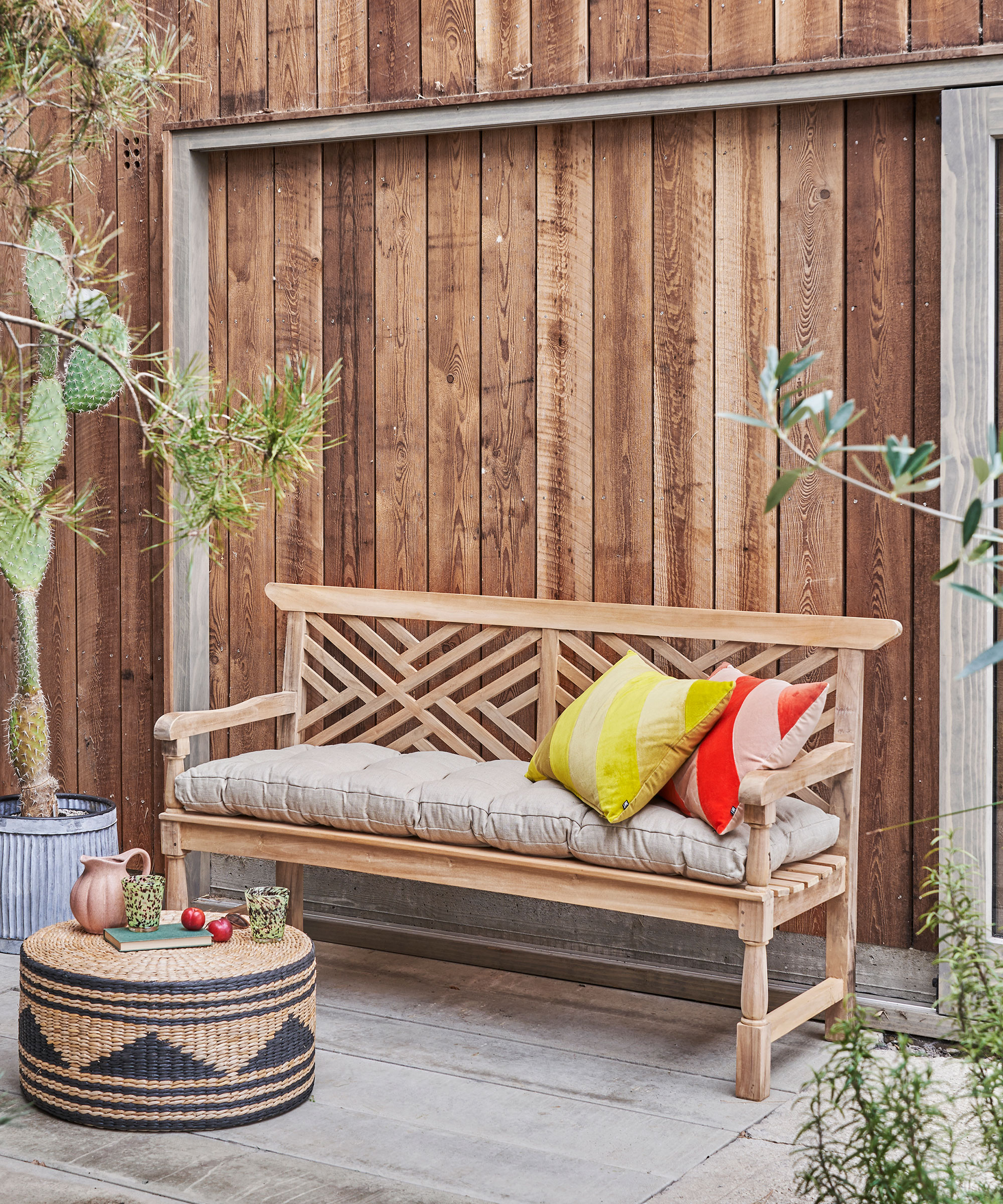 wooden garden bench with padded seat cushion on a patio in front of a wood clad wall