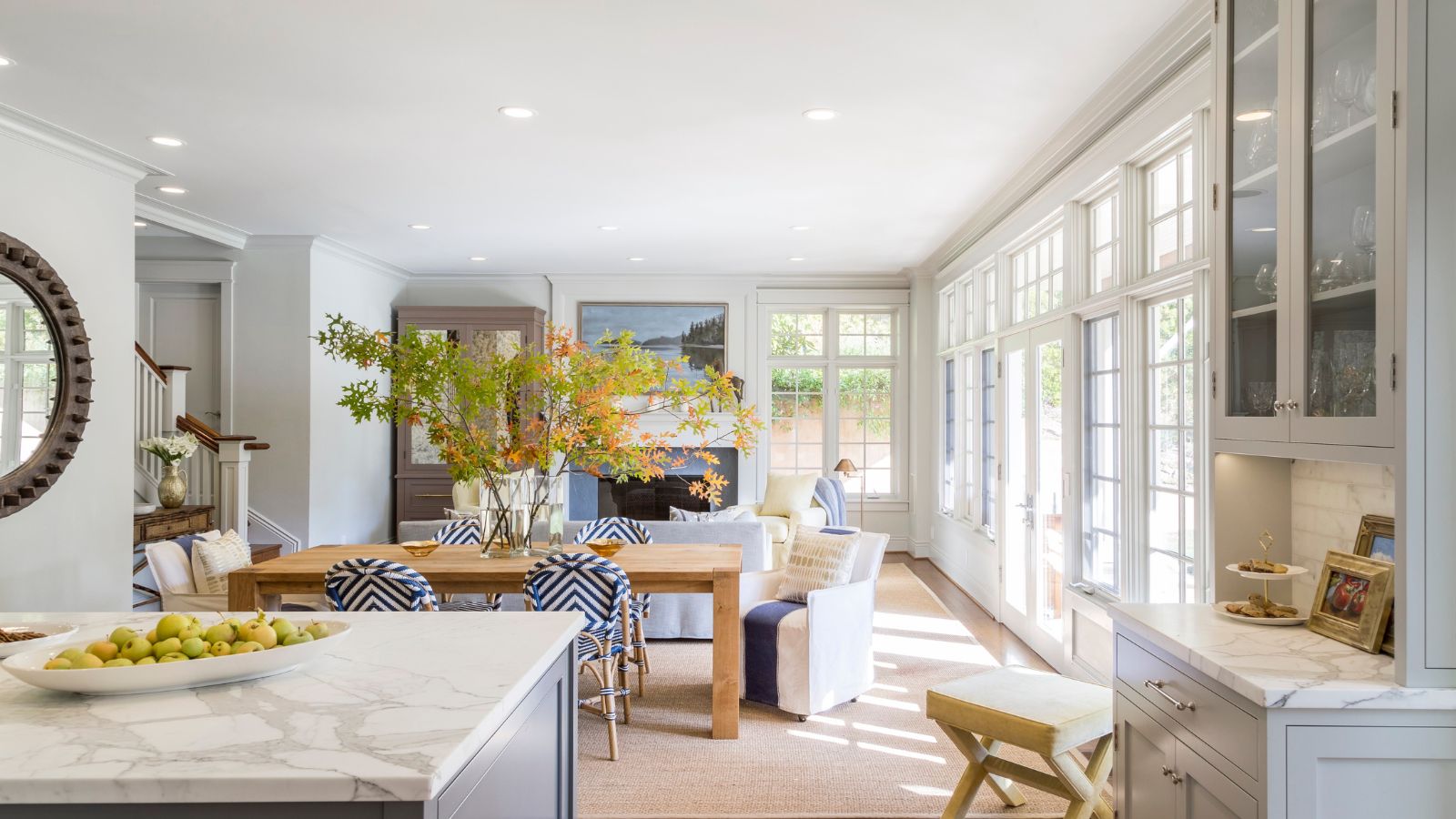 Open plan living room and kitchen with crittall doors, cabinetry painted in Benjamin Moore's Gray Owl, a marble island, a dining table with a vase of foliage, and a white sofa and armchair.