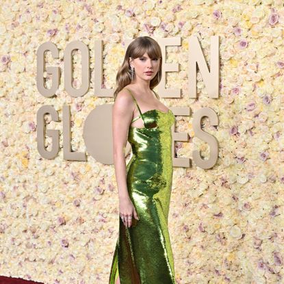 Taylor Swift poses in front of a flower wall with the words Golden Globes on it