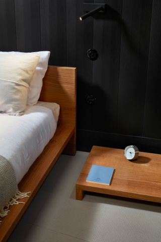 bedroom with black panelled wall, grey floor, a low wooden bed with white mattress and a low wooden side table