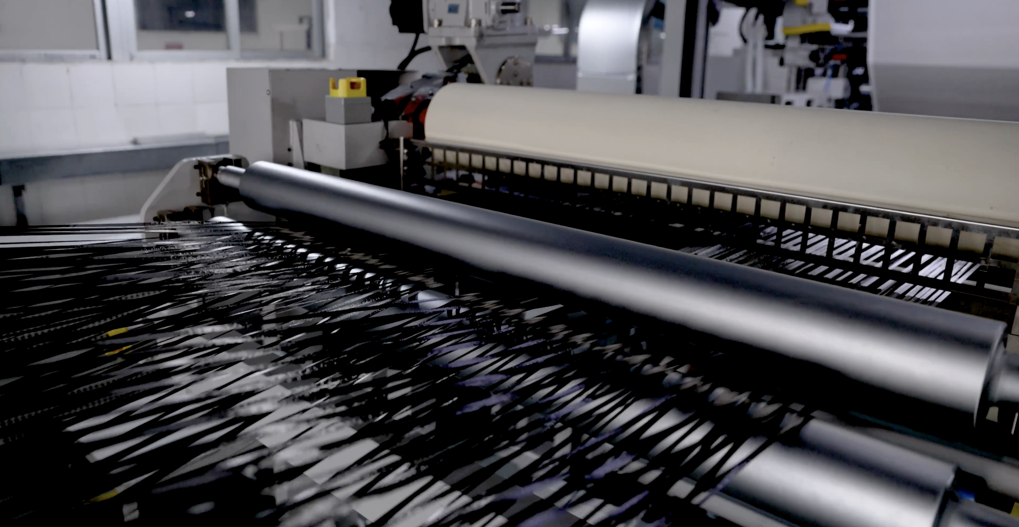 Strands of black carbon fibre going in to a machine with rollers