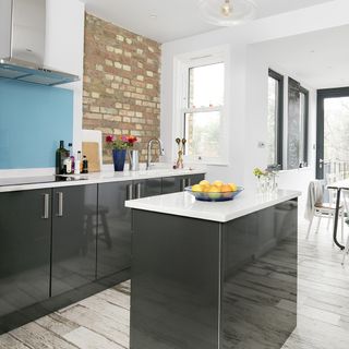 A kitchen with exposed brick and white walls with grey kitchen units, white worktops and an island
