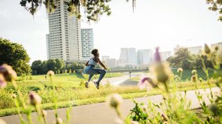 Woman squat jumping on running path in park beyond wildflowers