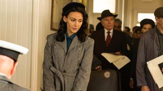 Kate (Michelle Keegan) wearing a grey overcoat and beret in line in Ten Pound Poms