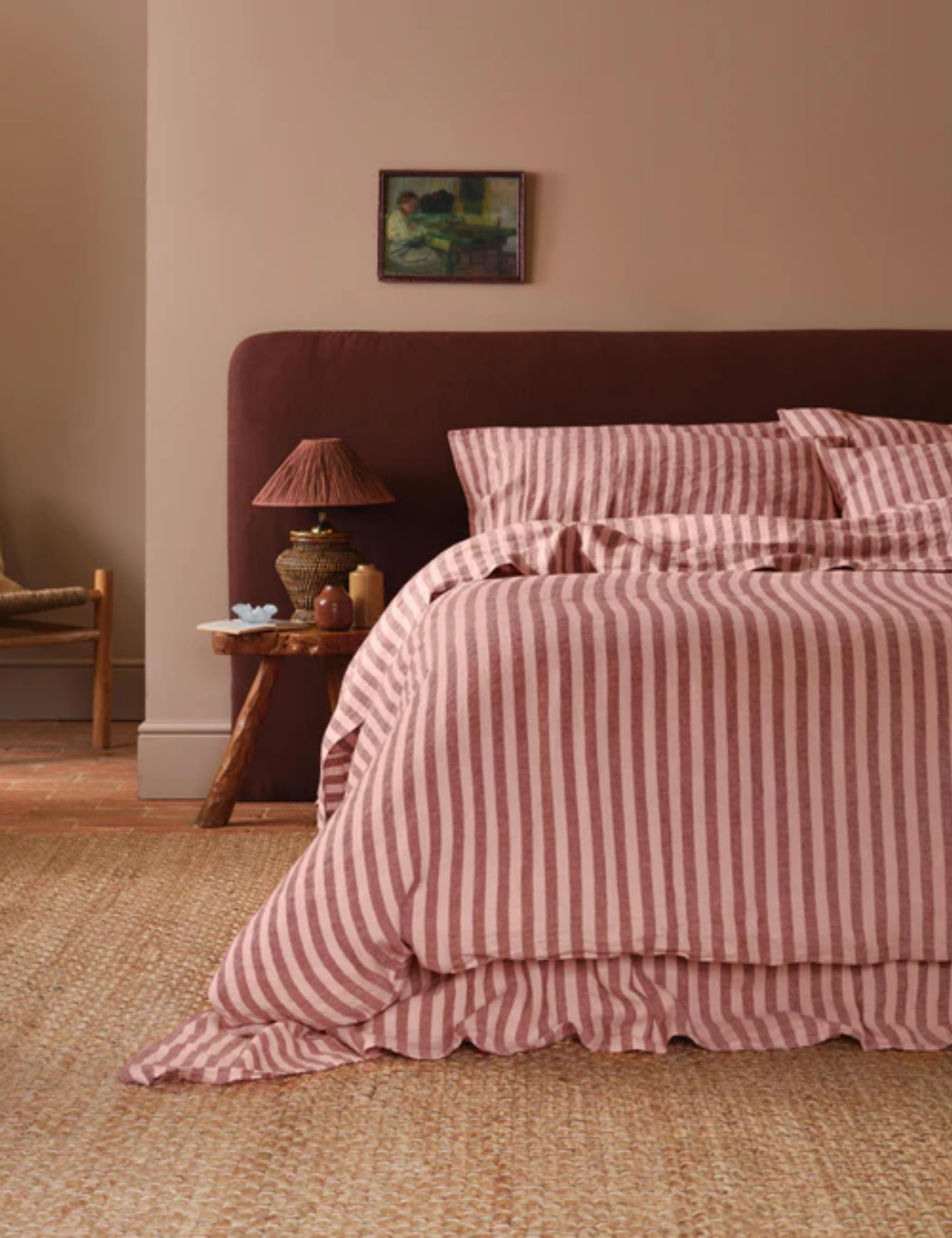 Cozy layered bedroom featuring an oversized oxblood headboard and berry cabana-striped bed sheets