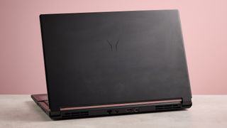 Rear three-quarter view of Medion Erazer Deputy 15 P1 open on desk with pink wall in background