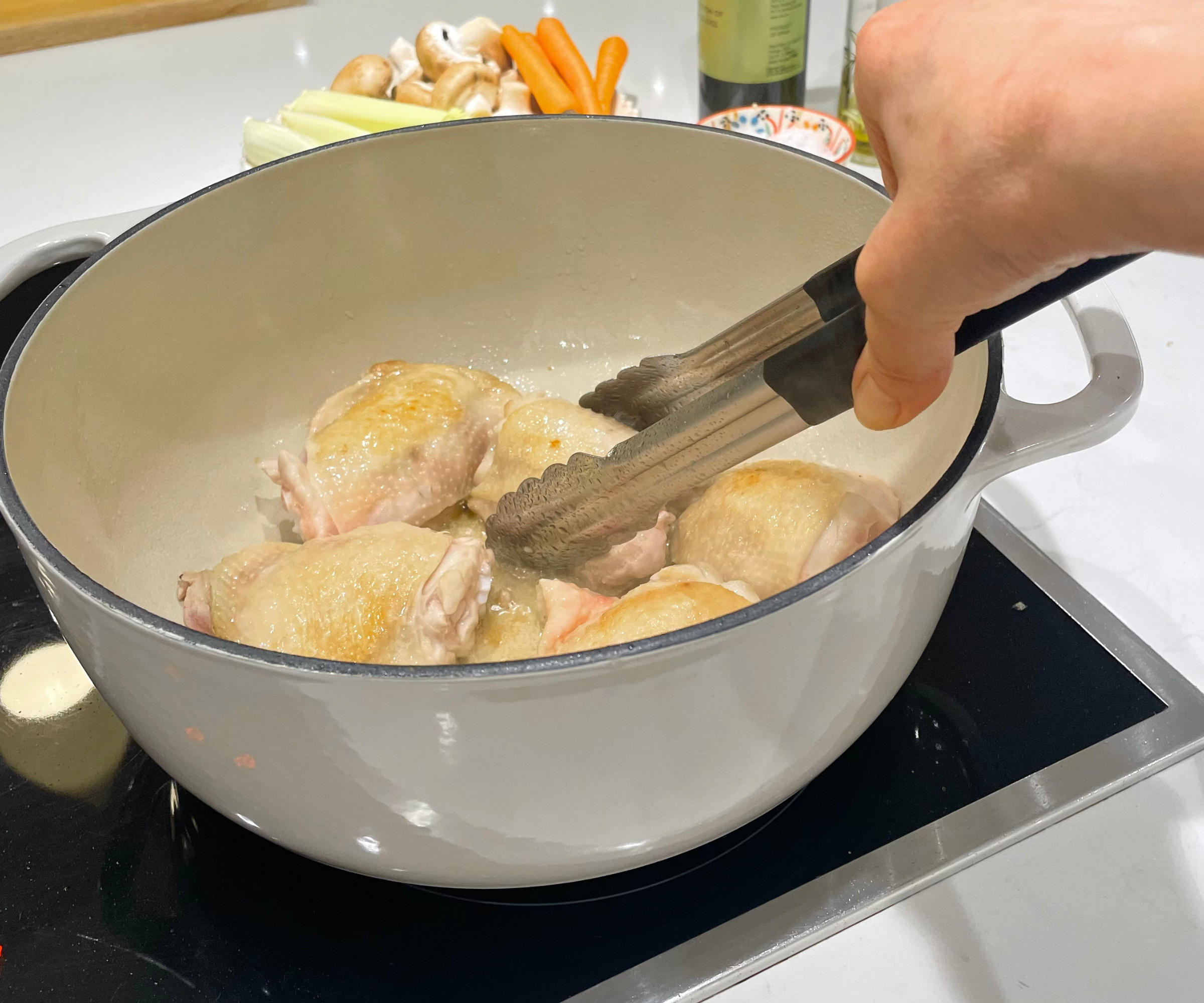 Sizzling chicken thighs and diced vegetables in the Lodge 6QT Enameled Cast Iron Dutch Oven with Lid in my test kitchen