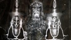 A black and white photo of a ripped brown cloth with impressions of a man with a beard wearing a crown in it