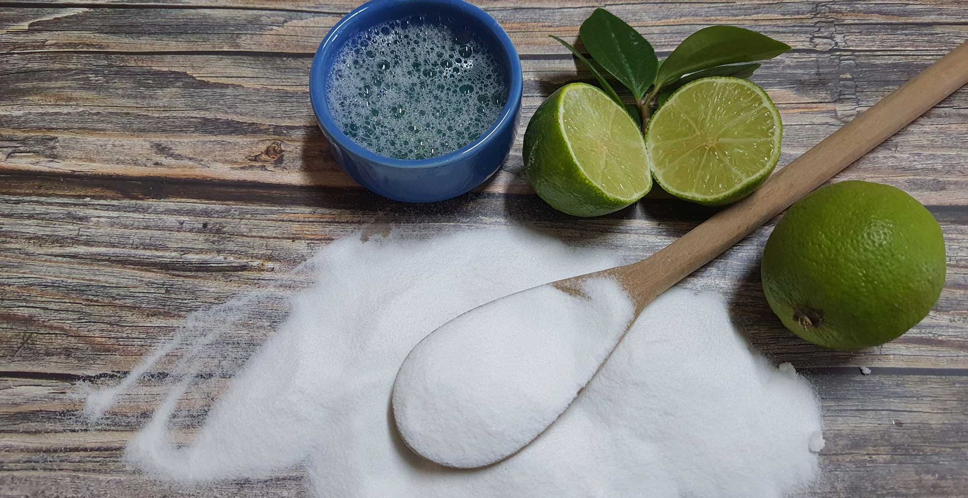 a wooden spoon on a kicthen counter with baking soda, lemon and vinegar to demonstarte how to clean wooden spoons with natural ingredients