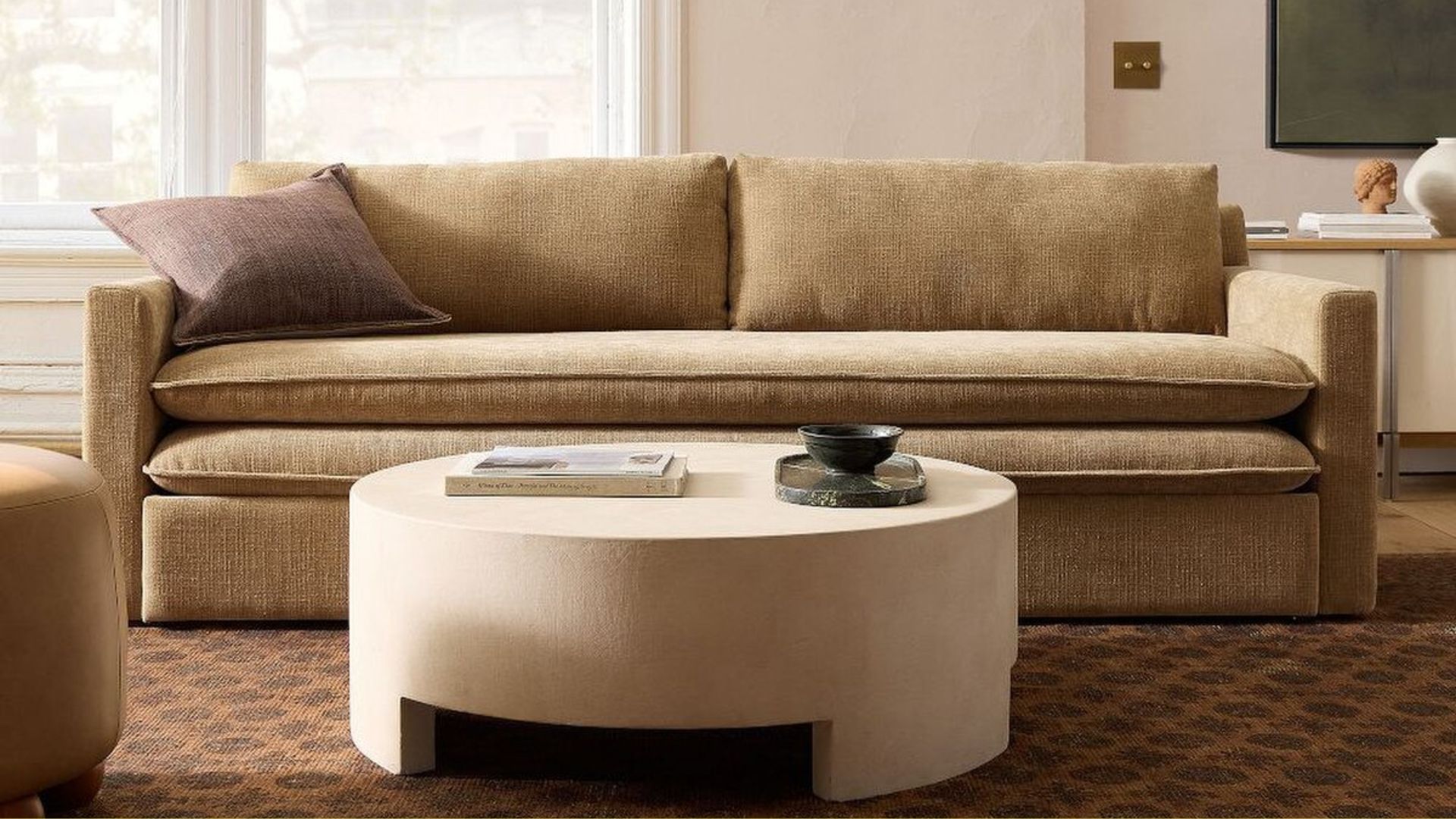 A sand-colored king-size sofa bed from West Elm in a living room with a round coffee table