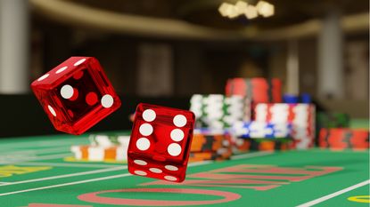 A pair of dice are in midair with a backdrop of chips on a craps table.