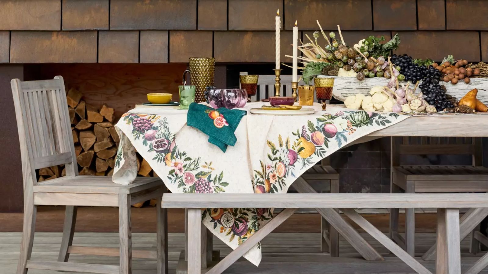 Outdoor Thanksgiving table with autumnal tablecloth, gold accents, and a fruit display