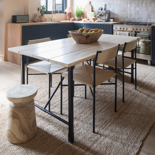 Wooden dining table and chairs on a neutral rug inside a kitchen