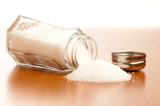 A salt shaker lies on table, with salt spilling out. 