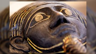 Close up of face on one of the sarcophagi found in a cache dating to the Egyptian Late Period (around the fifth century BC). The face is painted black with gold use to line the eyes, beard, and headpiece.
