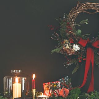 A Christmas wreath with a big red bow hung on the wall above a decorated fireplace mantelpiece