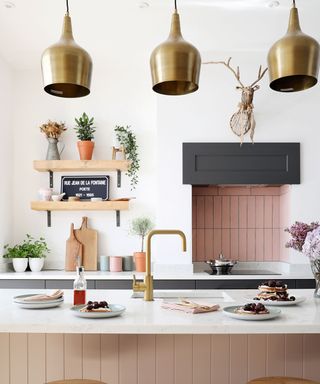 Pink kitchen island with brass tab and coordinated brass pendants