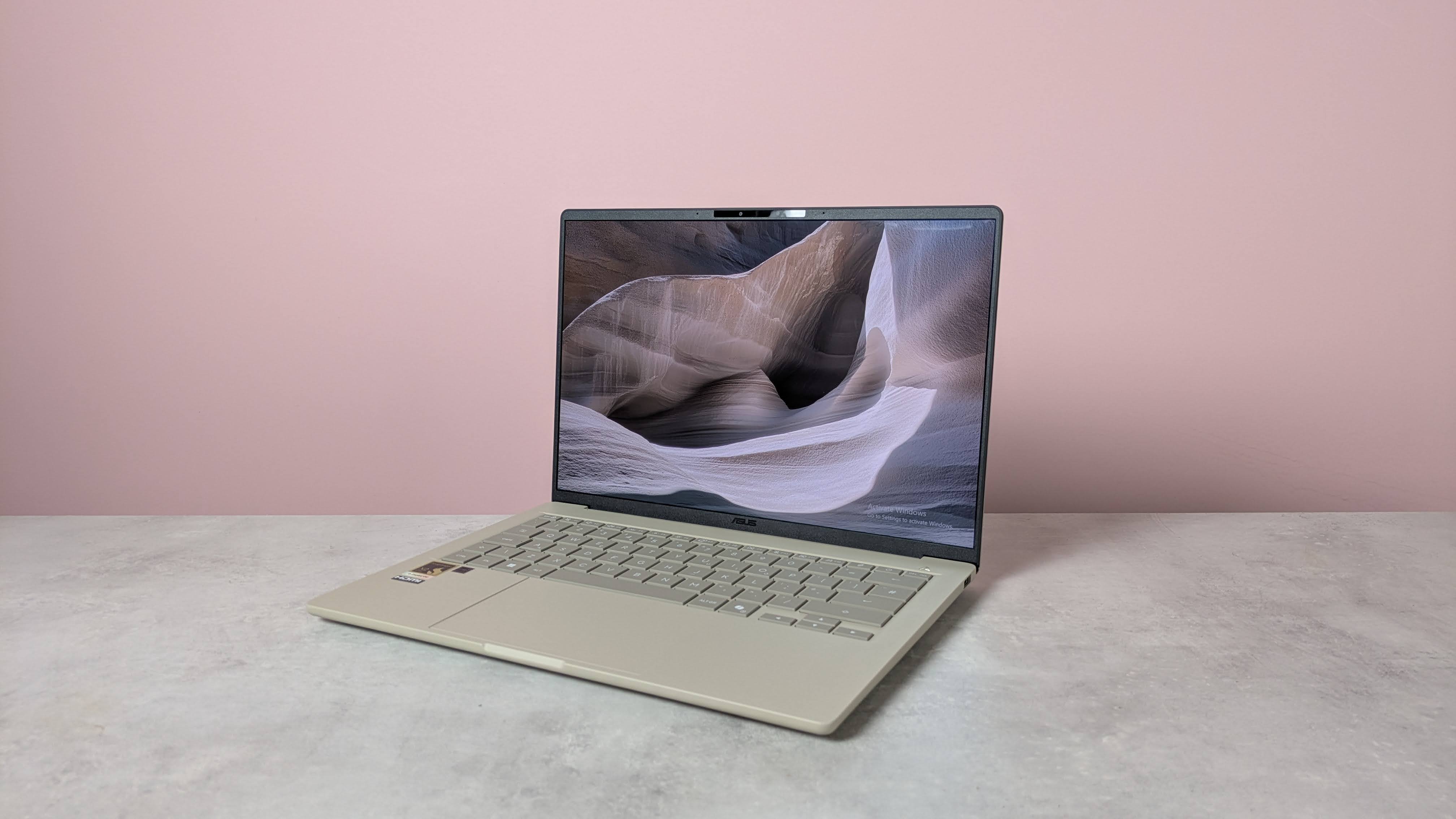 Three-quarter view of Asus Zenbook A14 open on a desk with pink wall in background