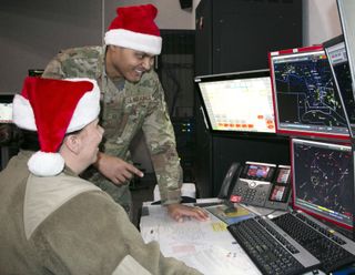 Air Force Master Sgt. Brian Burgess, standing, and Maj. Bonnie Bosworth of the New York Air National Guard’s 224th Air Defense Squadron train for Santa tracking operations on Dec. 16 at the NORAD Eastern Air Defense Sector headquarters in Rome, N.Y.