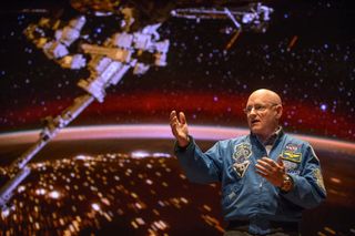 Astronaut Scott Kelly stands in front of a screen showing the International Space Station over Earth