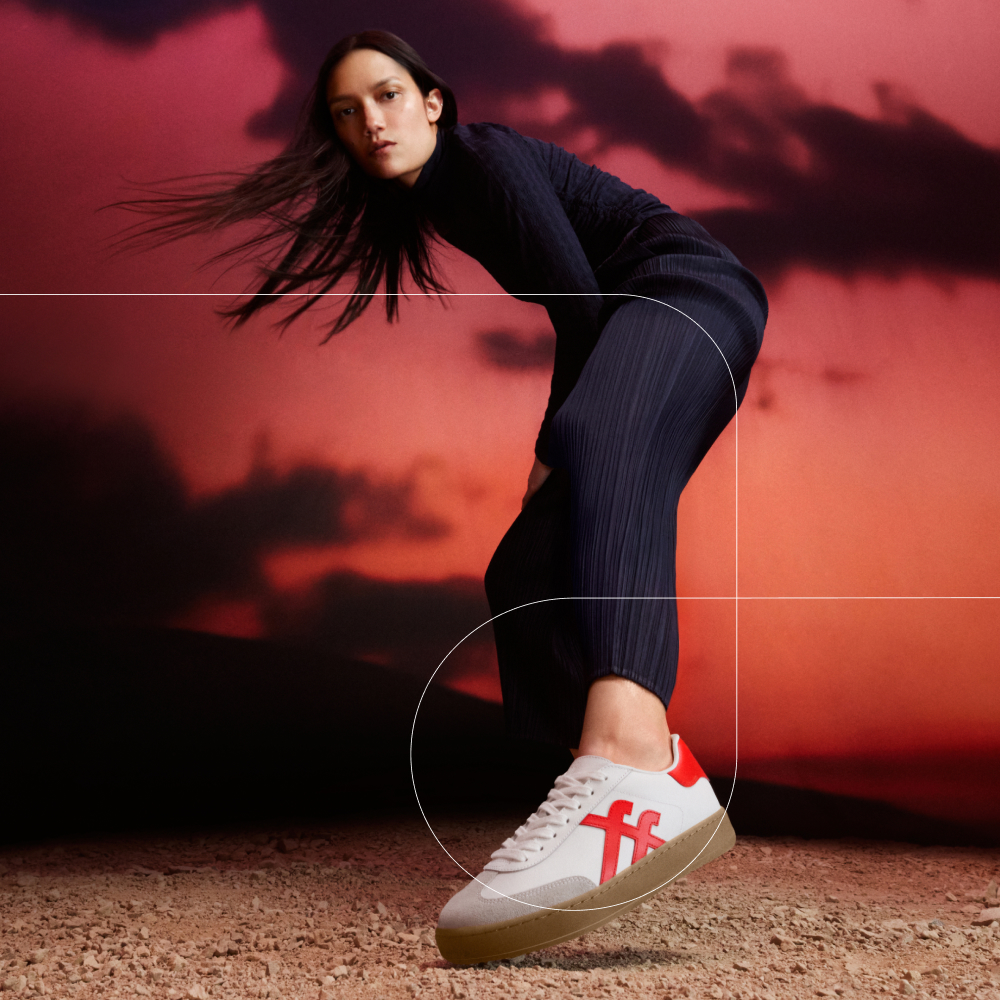 Model wearing White FitFlop trainers with red stripes against a red sky background
