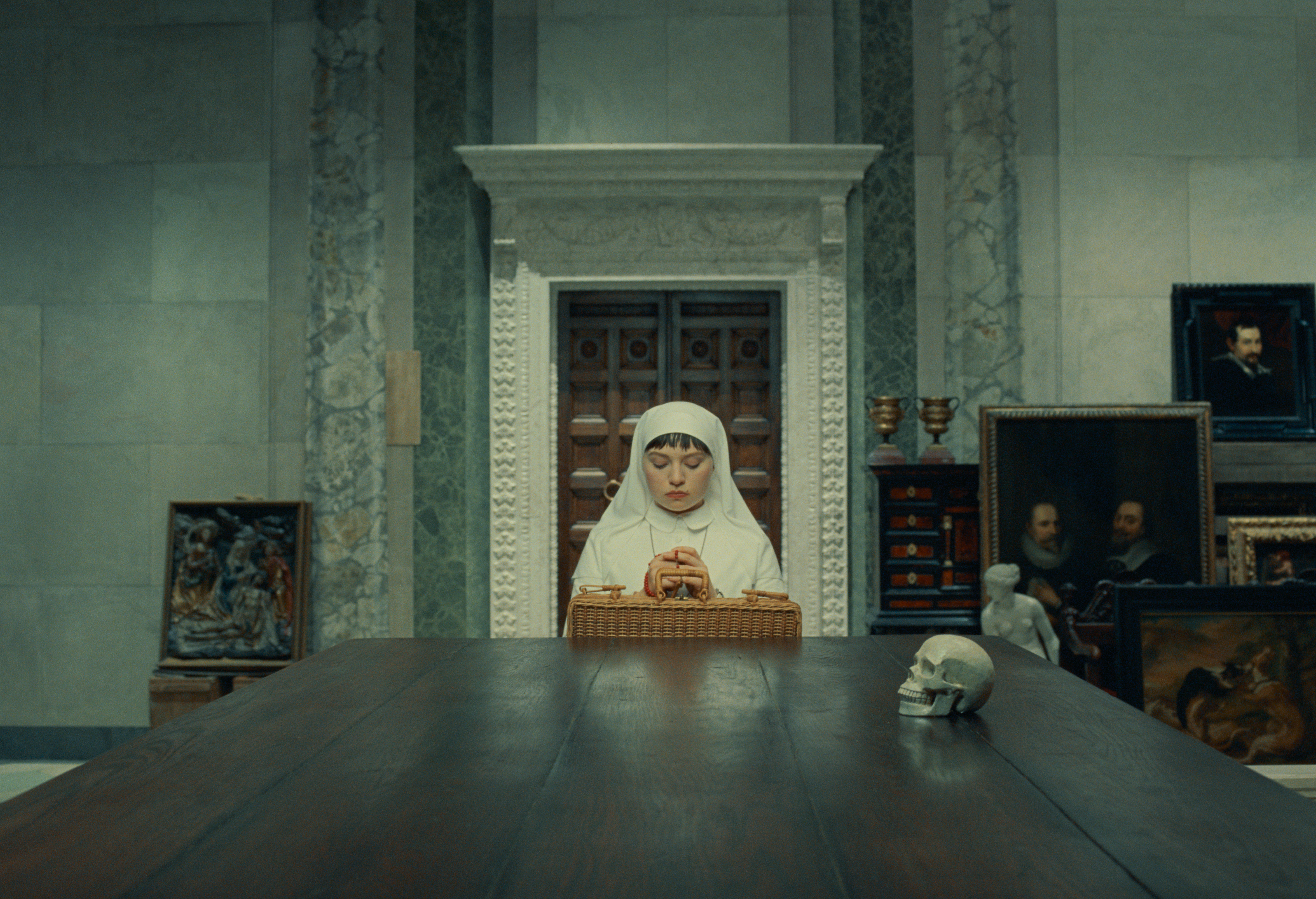 mia threapleton as liesl sitting at a table as she reconnects with her father for the first time in years in the phoenician scheme