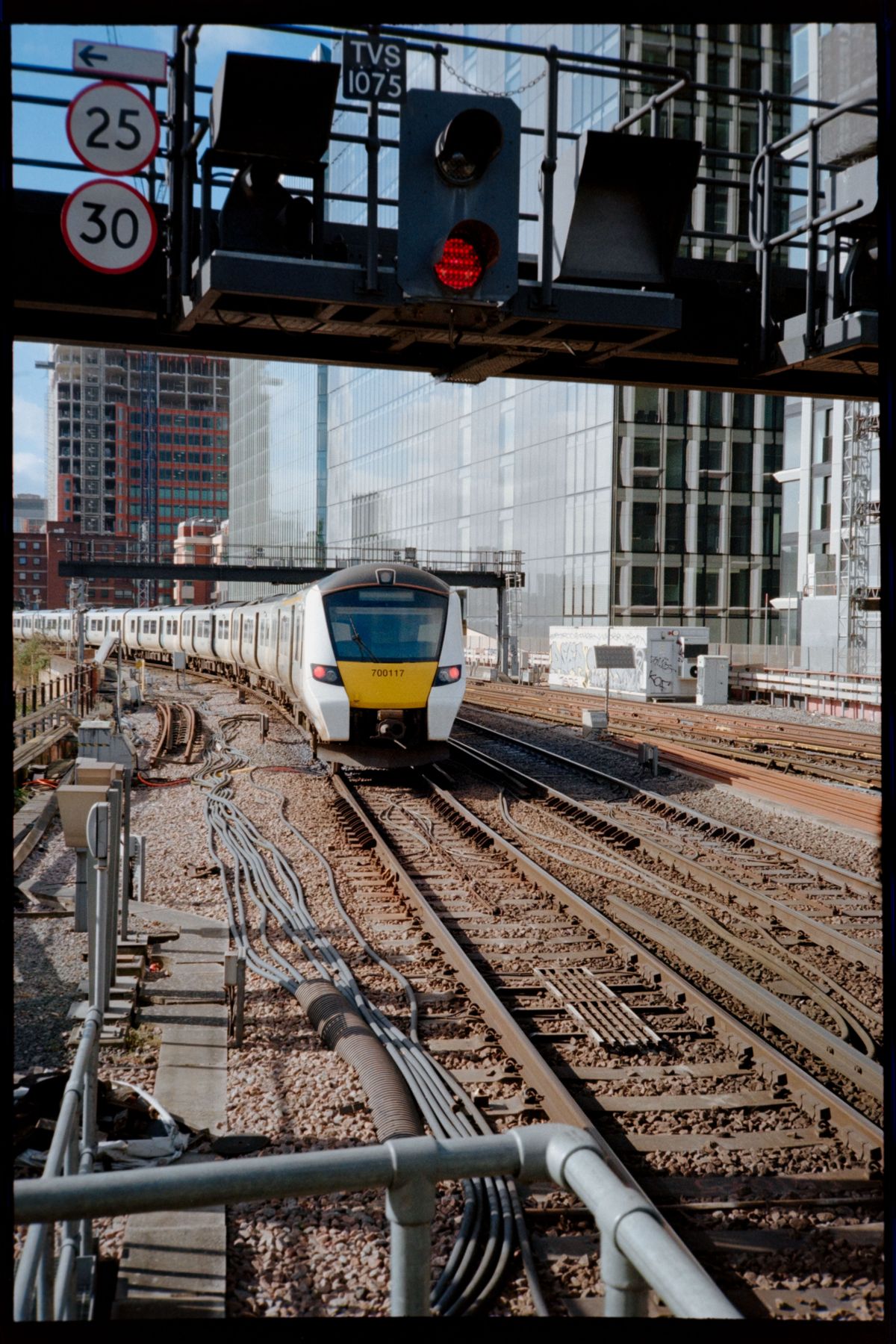 A modern train passing under a red railway signal on tracks surrounded by city buildings.