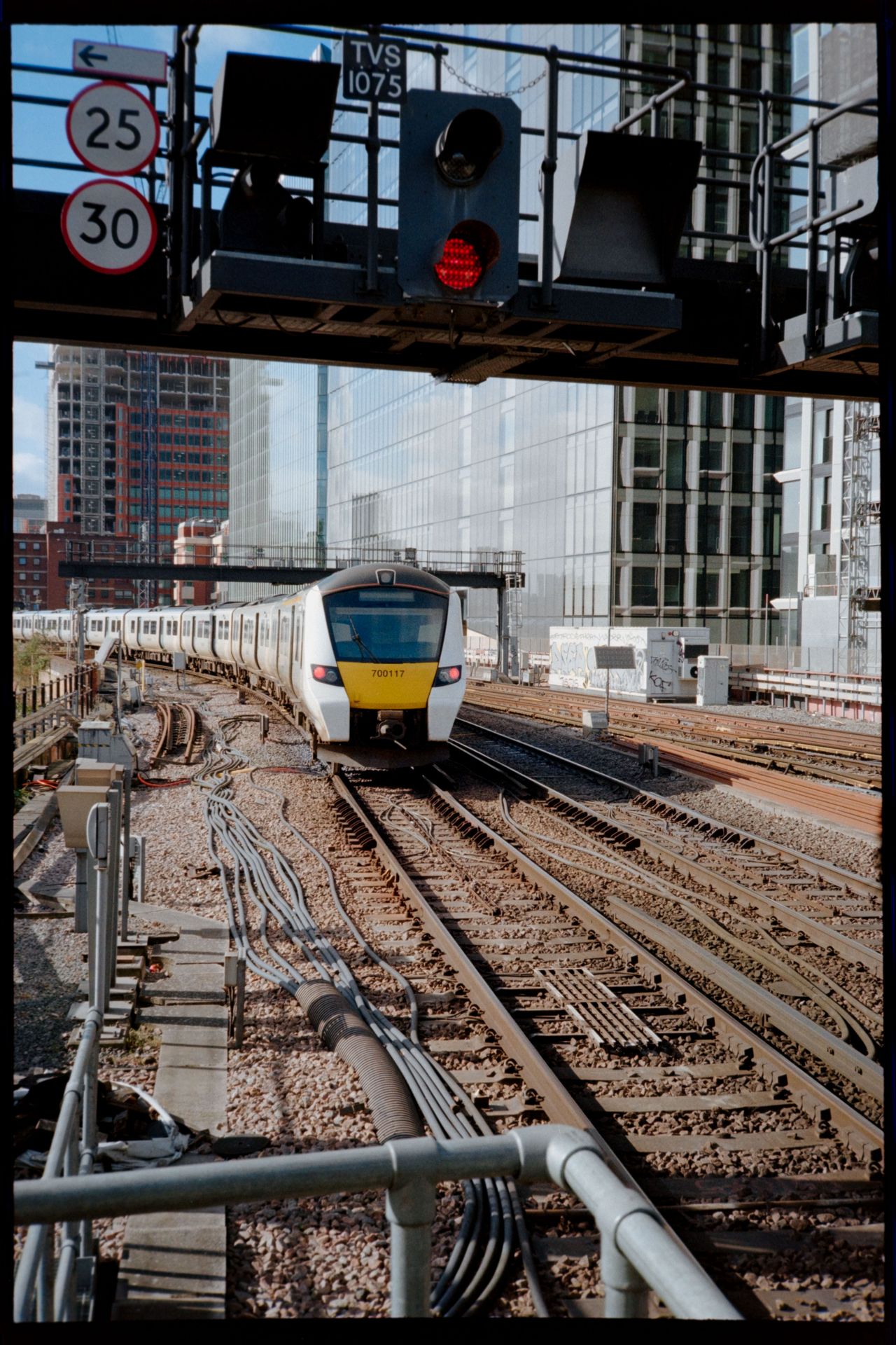 A modern train passing under a red railway signal on tracks surrounded by city buildings.