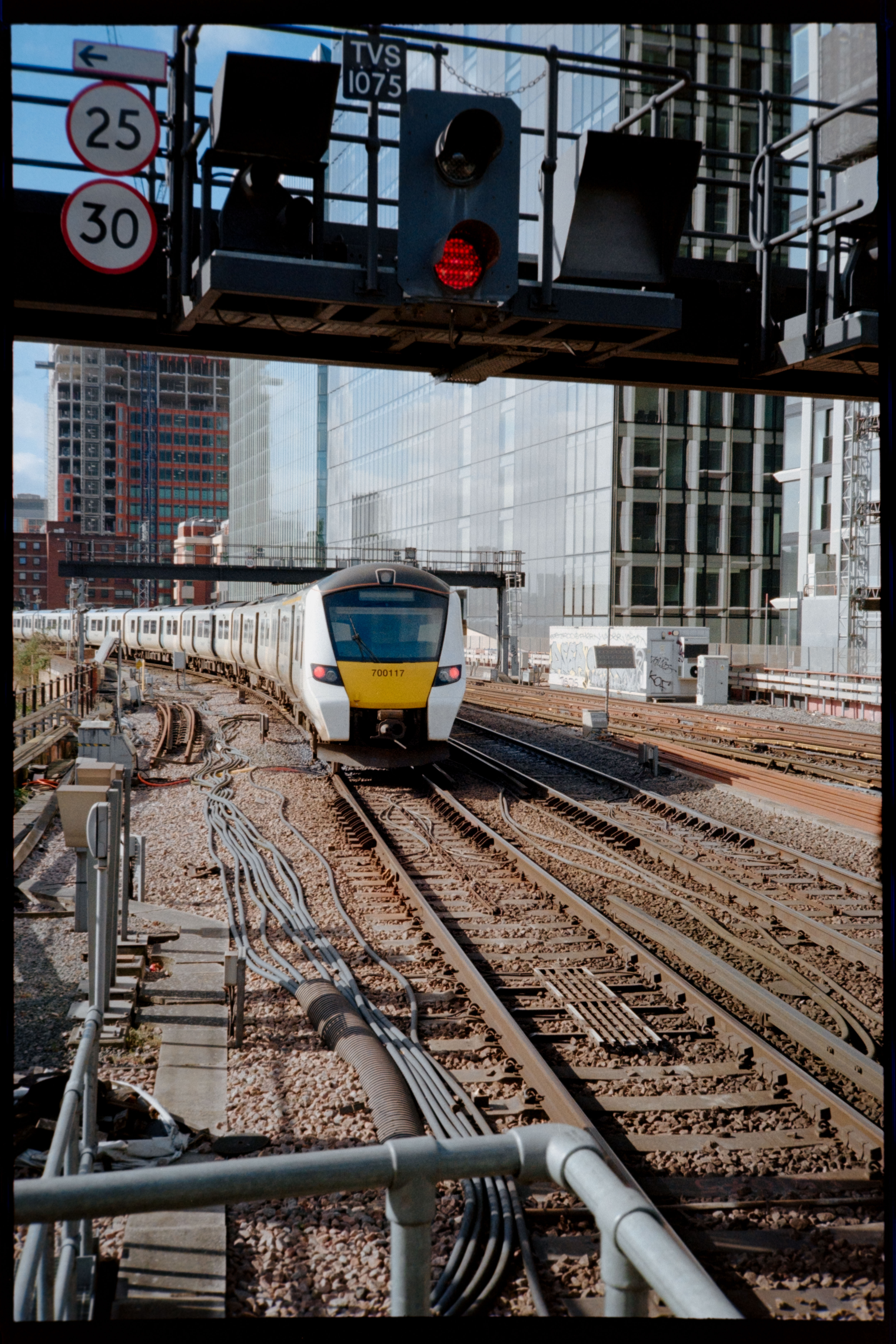 A modern train passing under a red railway signal on tracks surrounded by city buildings.