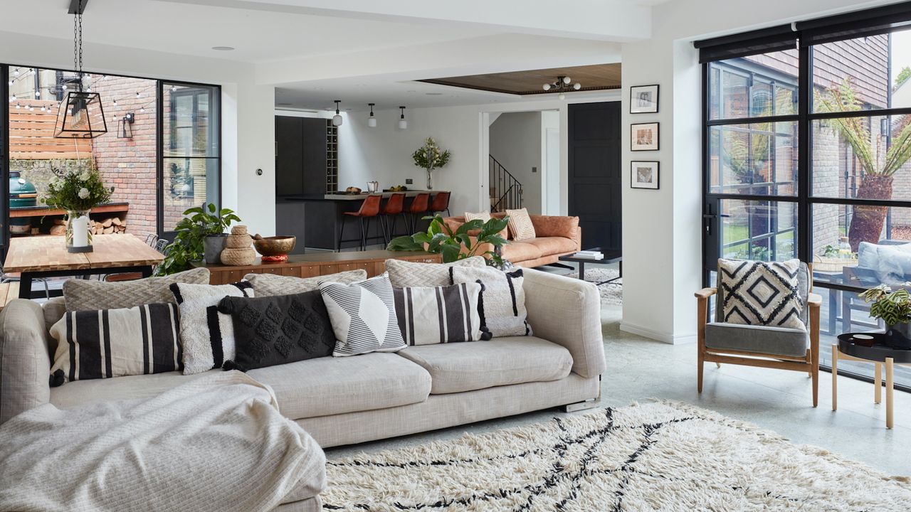 Open plan white living room with beige sofa with black and white cushions