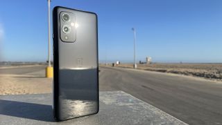 A OnePlus 9 from the back, standing next to a road