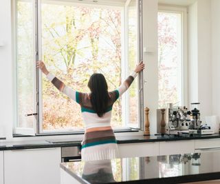 woman stood with back to camera opening large windows in kitchen