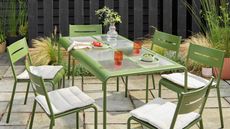 a green outdoor table with a glass top and green chairs in a modern garden