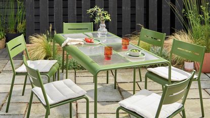 a green outdoor table with a glass top and green chairs in a modern garden