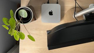 A bird view of the Mac mini on a desktop, surrounded by monitor, speaker and a plant.