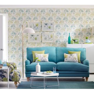 living room with blue sofa set having yellow and white cushions and floral printed walls
