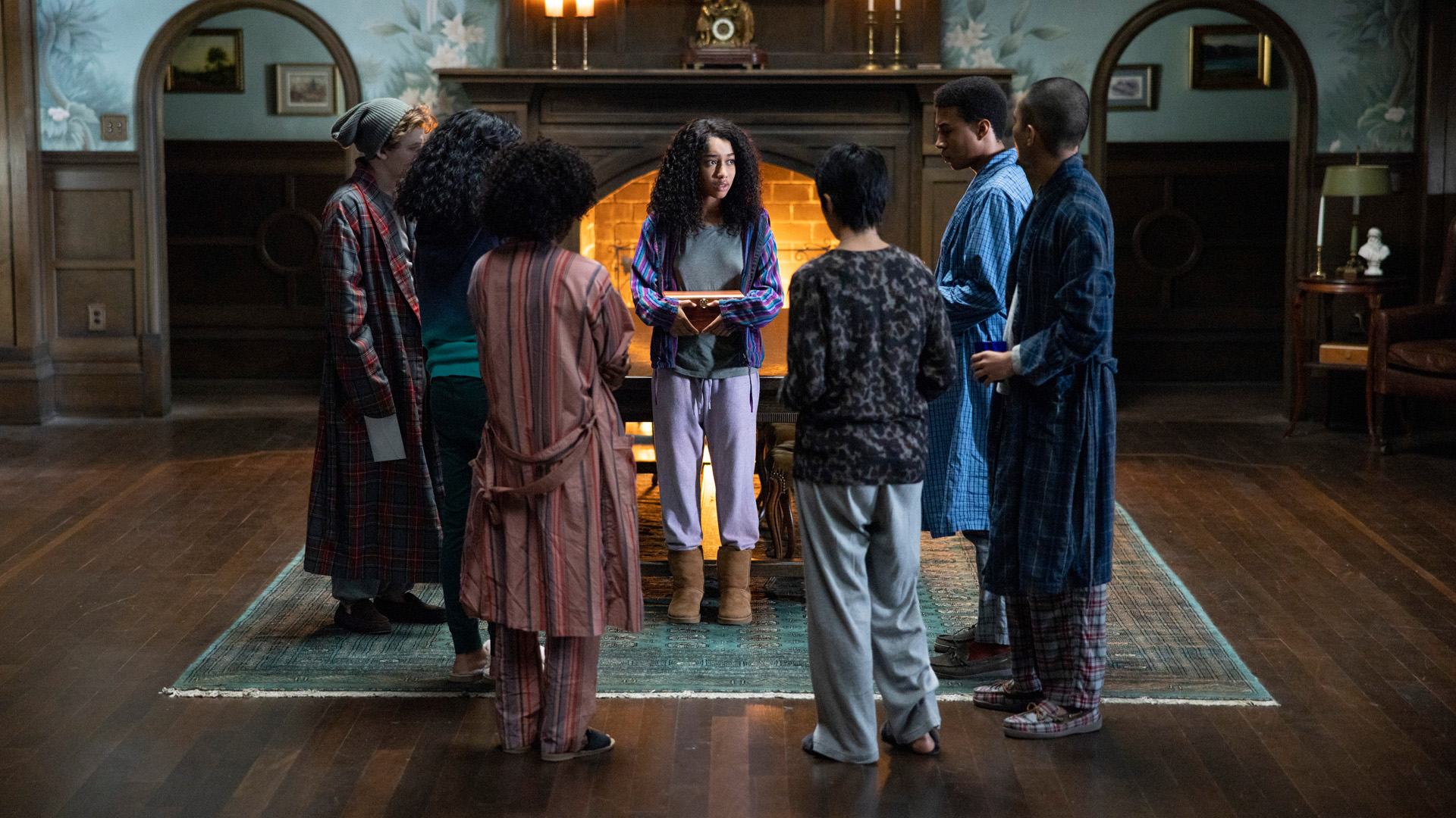 The members of The Midnight Club stand in a circle next to a roaring fire in Netflix's TV adaptation of the mystery-thriller novel