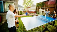 A family plays ping pong outside in a backyard.