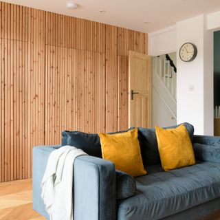 A living room with a wood-panelled baton wall and a blue velvet sofa with yellow cushions