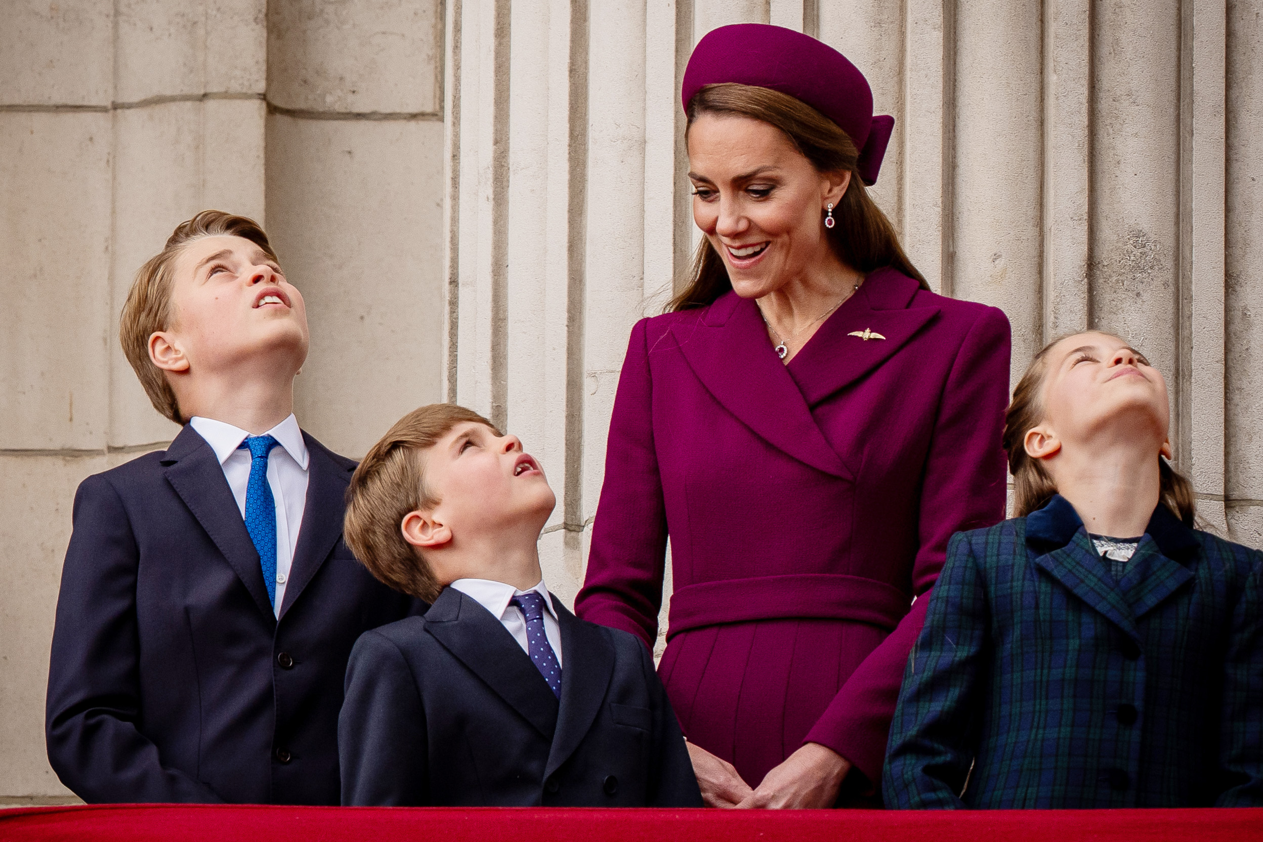 Princess Kate smiling at Prince Louis, who is looking up at planes with Prince George and Princess Charlotte