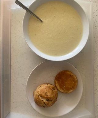 A prepared leek and potato soup with rosemary and sea salt bread roll on plastic tray