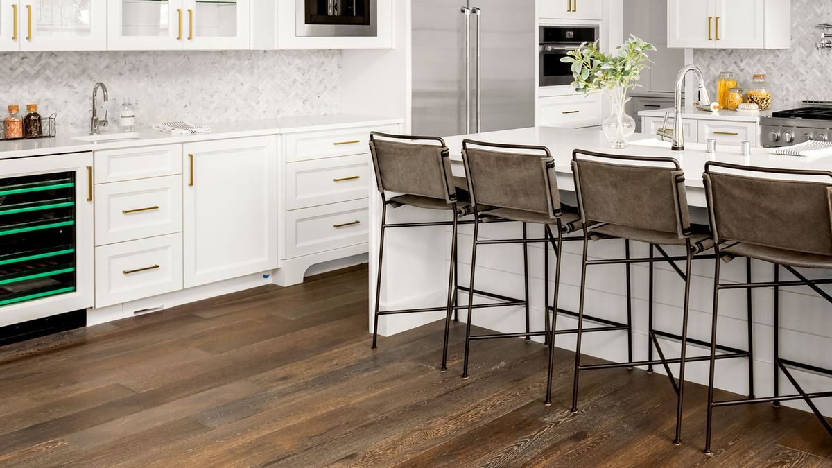 Contemporary white kitchen with dark wooden flooring and island with high back chairs