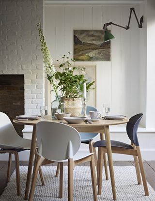round wooden table with matching wood chairs on textured neutral rug in a small dining room/kitchen with an open brick front fireplace