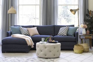 A blue L-shaped storage couch for a small living room with large windows, pale blue and neutral decor and a gold floor lamp.